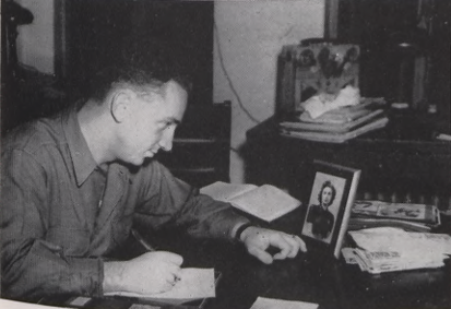 Student writes a letter while looking at photo on desk.